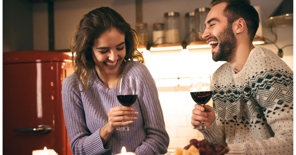 How to hold a wine glass - Couple laughing in the kitchen while holding glasses of wine